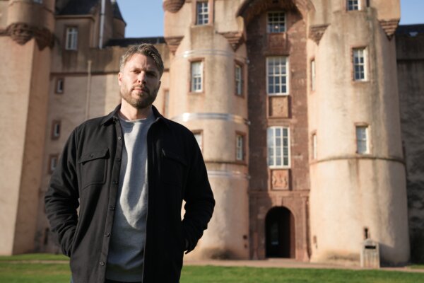 A man standing in front of a historic castle building on a sunny day.