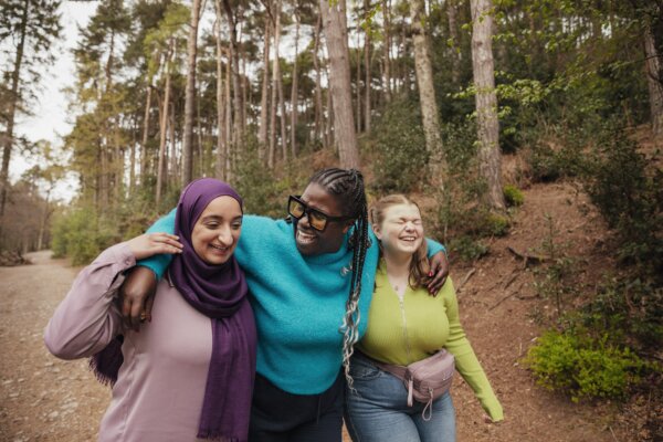 Three young people embracing and laughing while walking along a forest path.