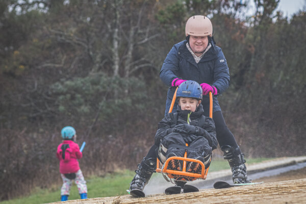 A young member in a sit ski on the slope at Pembrey, supported by a guide.