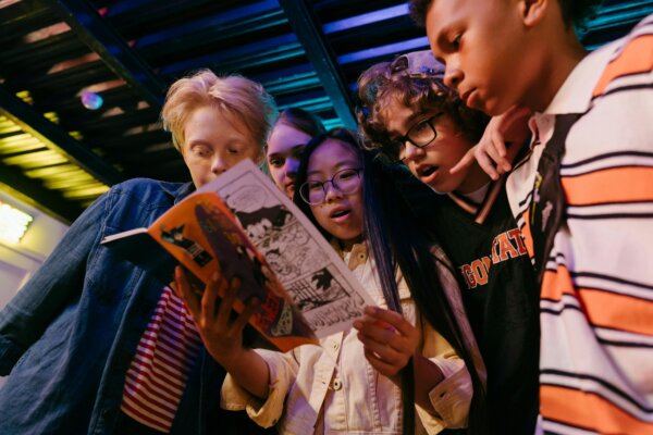 Five young people are standing around one of them that is holding a book.