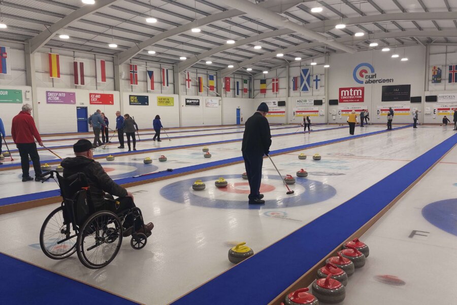 Wide view of the main ice hall at Curl Aberdeen, showing all six international-standard sheets in use. A wheelchair curler in the foreground reflects the club's fully inclusive offer, with members of all abilities competing together in the regular league. Image credit: Curl Aberdeen