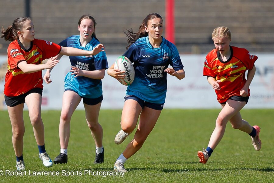 Four young rugby players during a match, with one player holding a rugby ball.