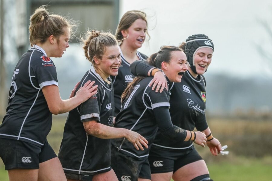 Five people in sports jerseys embracing with gleeful expressions during a training session.