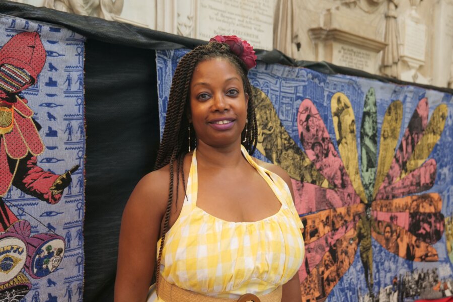 A person stands in front of a colourful textile artwork.