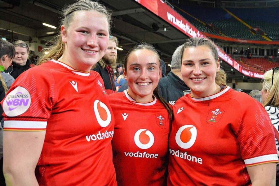 Three rugby players in red jerseys posing for a photo.
