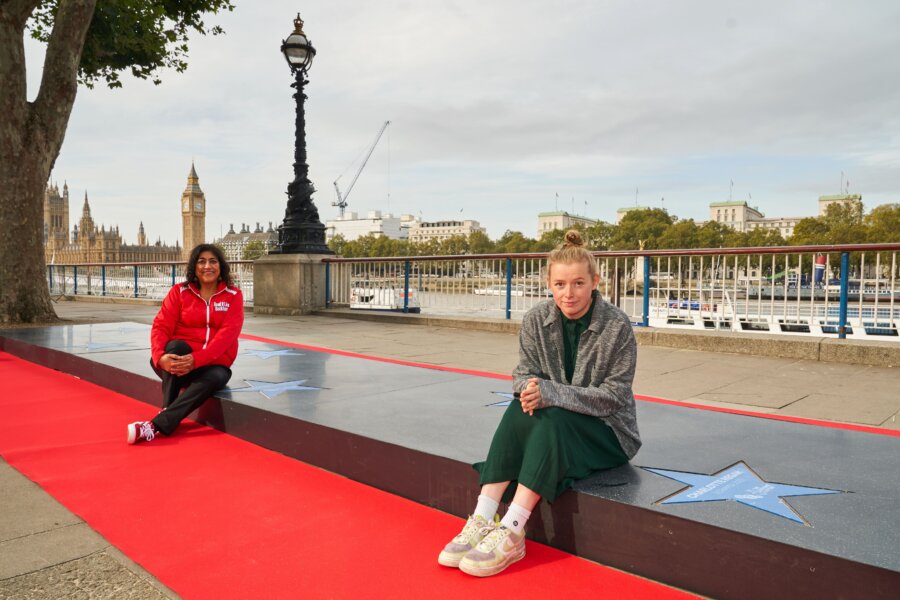 Two women, Gurinder Chadha OBE and Charlotte Regan, sitting down in the The National Lottery ‘walk of stars’ installation in London