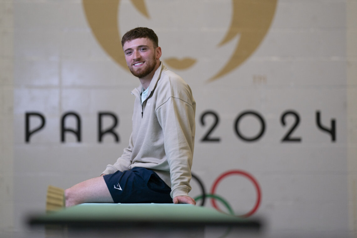 A man (Matty Lee) sit down infornt of a Paris 2024 mosaic