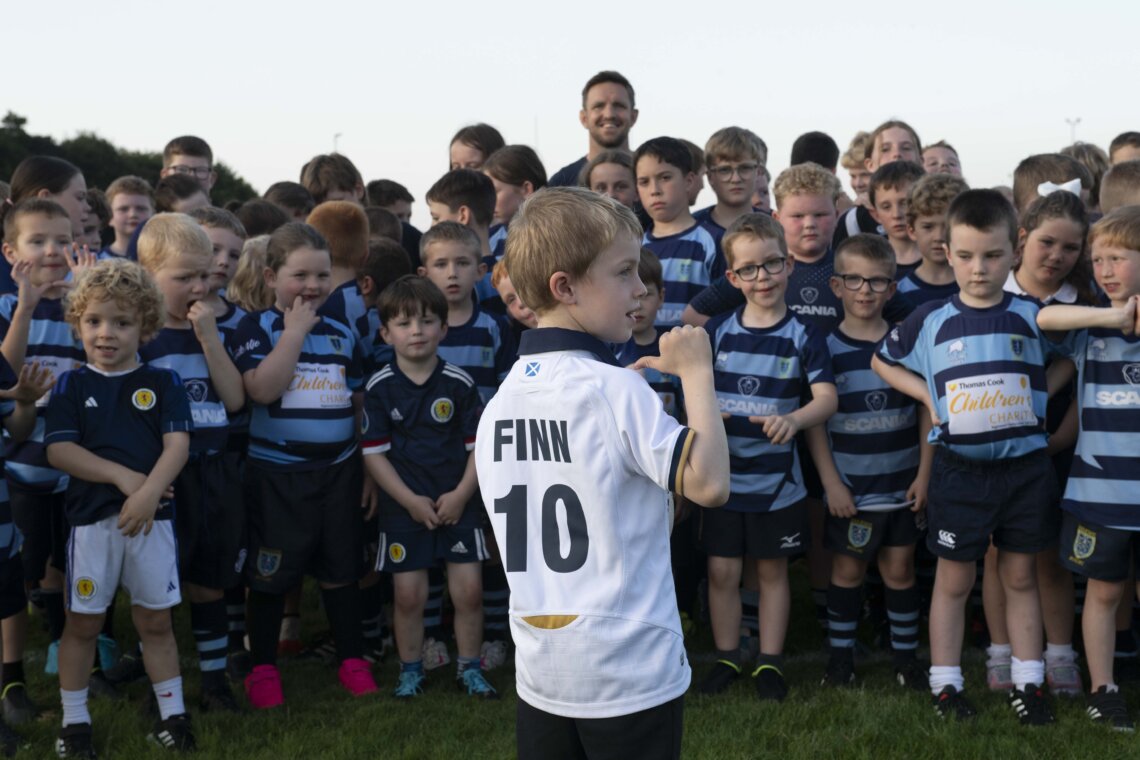 A man (Rory Lawson) surronded by children of the  Falkirk RFC in a field.