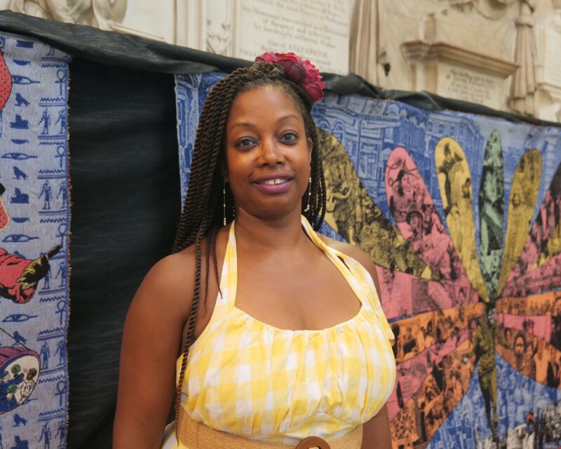 A person stands in front of a colourful textile artwork.