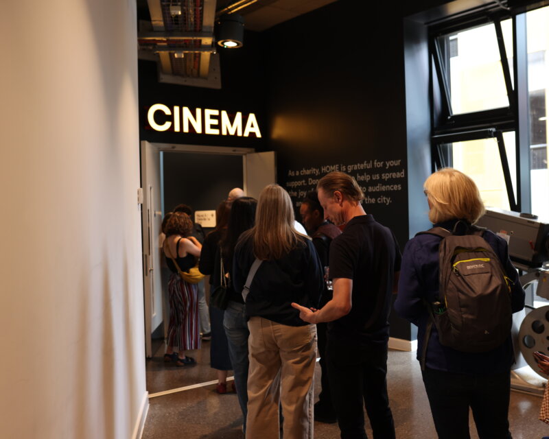 People queue up in front of a room with a sign that says 'cinema'.
