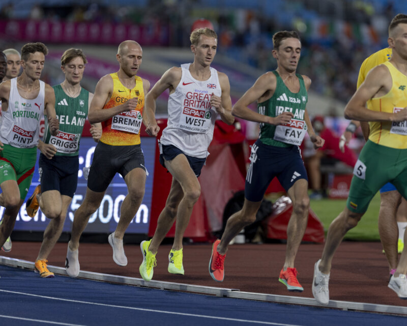 A group of male athletes in professional running kit race around a track.