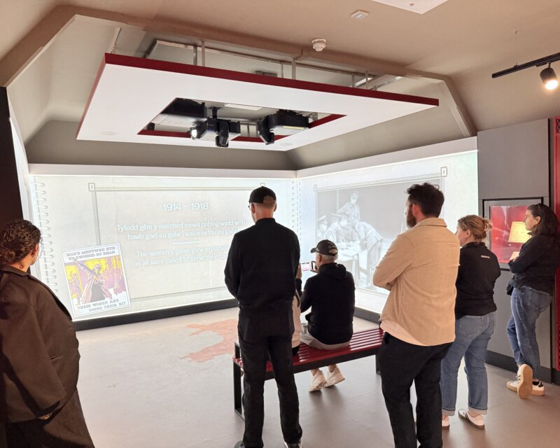 People stand in a room with a visual exhibition on the wall.
