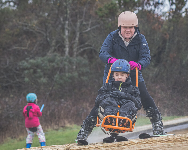 A young member in a sit ski on the slope at Pembrey, supported by a guide.