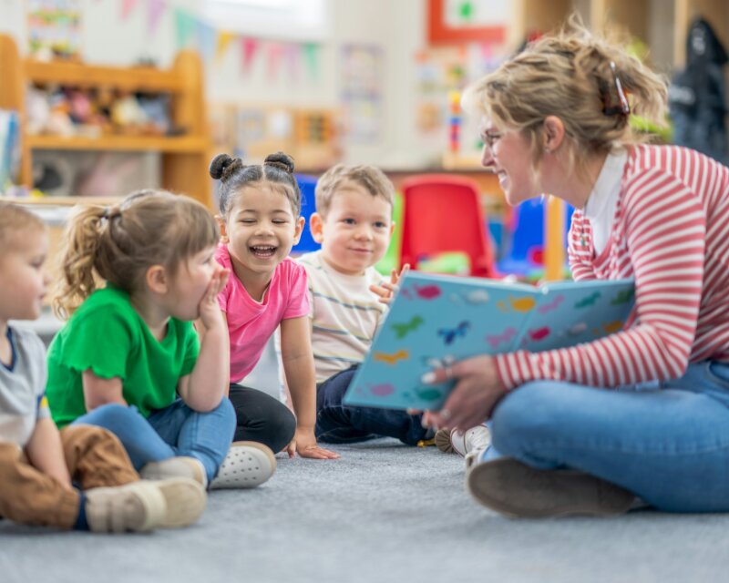 A group of children are being read a story by a teacher in a library.