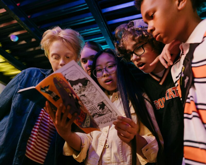 Five young people are standing around one of them that is holding a book.