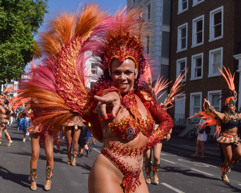 A lady in colourful carnival costume leads a group of dancers.