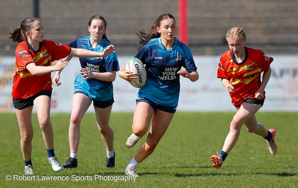 Four young rugby players during a match, with one player holding a rugby ball.