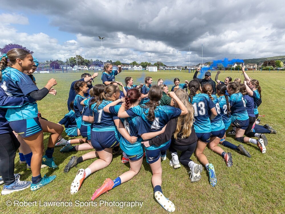 A group of young rugby players in a group huddle, cheering.