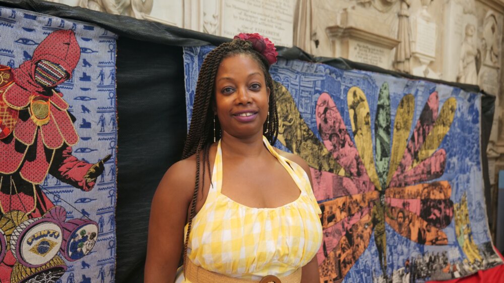 A person stands in front of a colourful textile artwork.