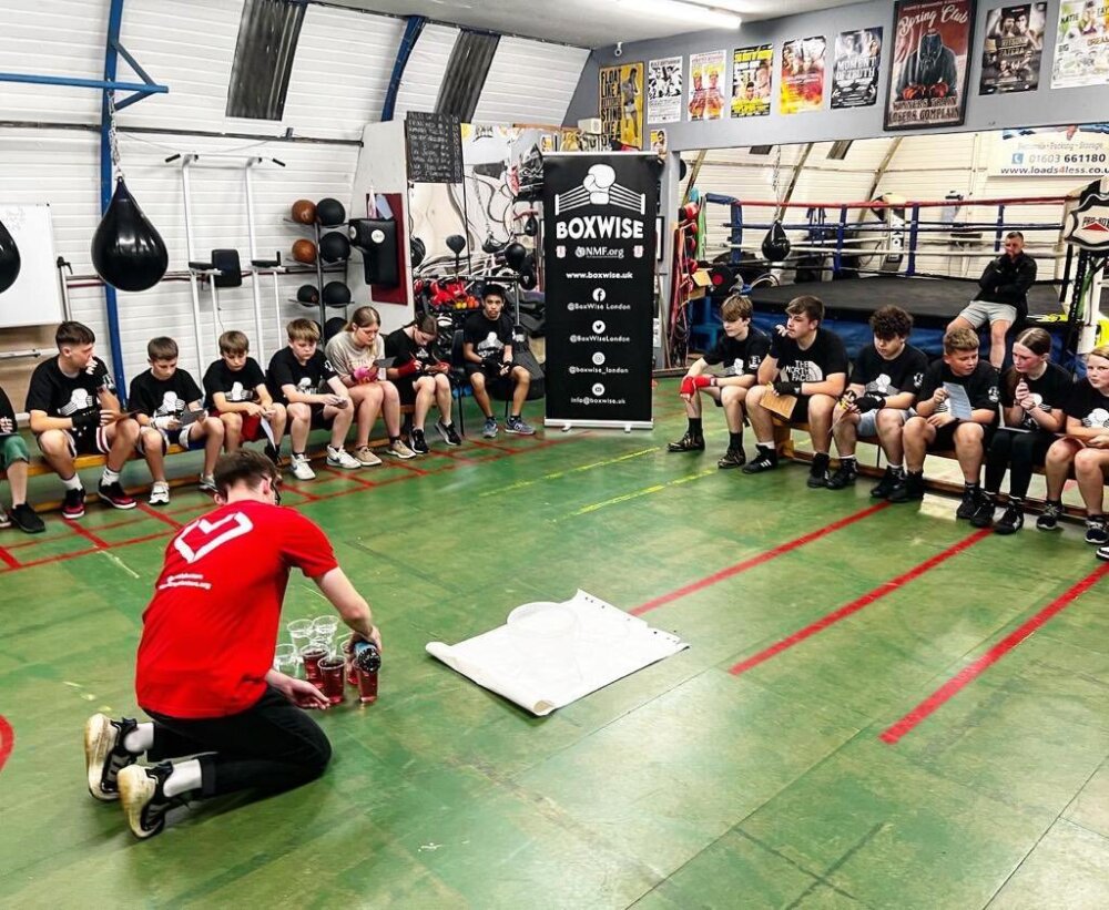 A medic pours cordial, representing blood, at a Street Doctors session in a boxing club. (Photograph by Street Doctors, 2023)