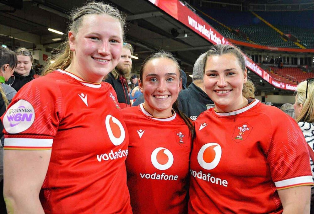 Three rugby players in red jerseys posing for a photo.