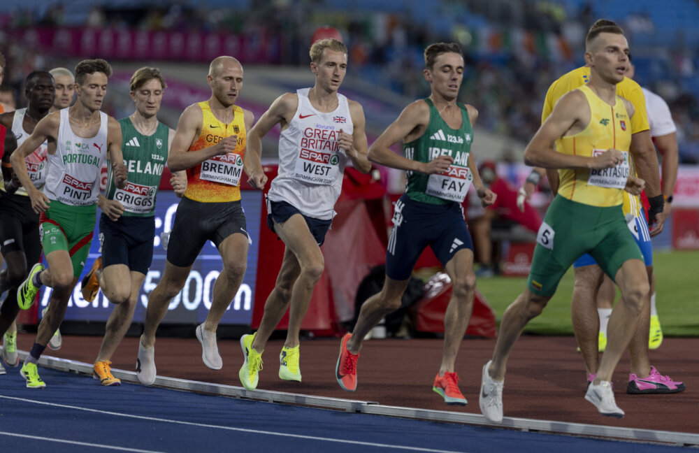 A group of male athletes in professional running kit race around a track.