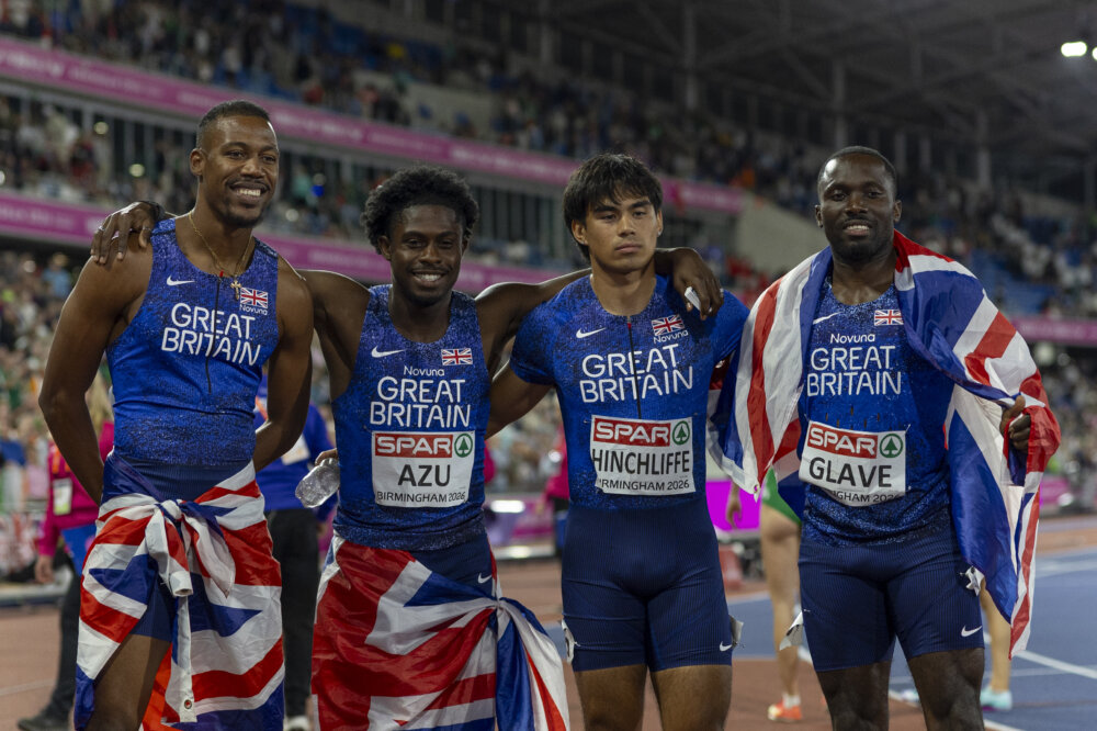 Four athletes in kit that says 'Great Britain' are posing for a photo. They're wearing Union Jack flags.