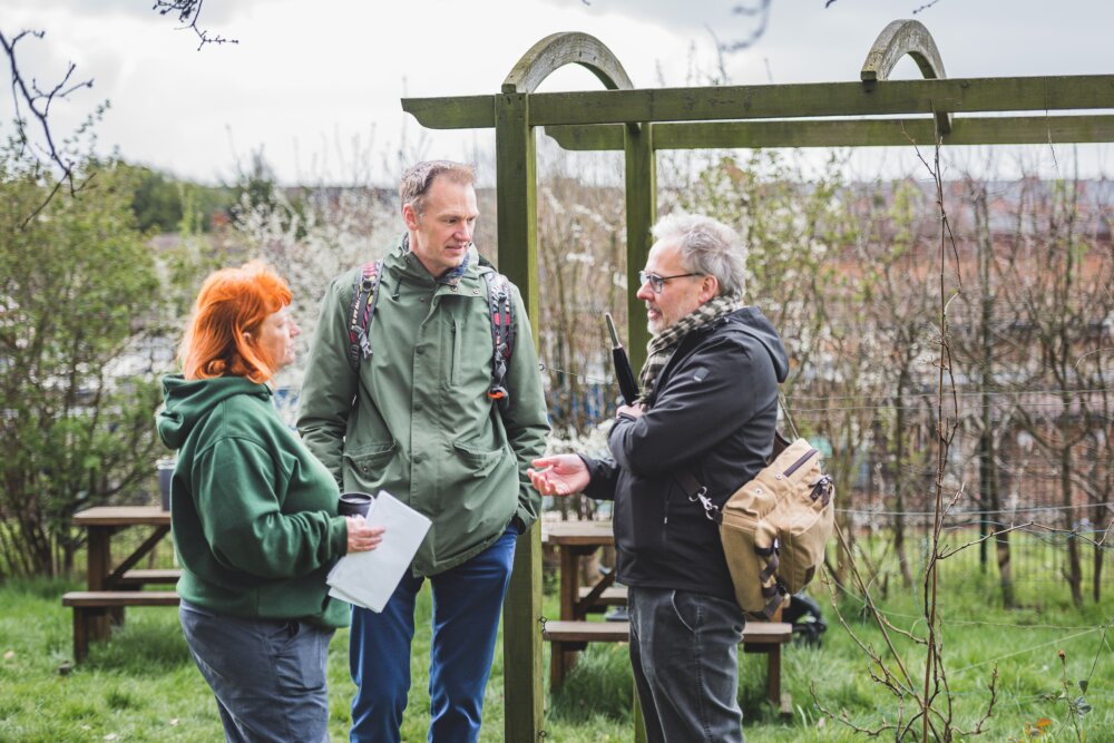 Three people standing in a garden, having a conversation.
