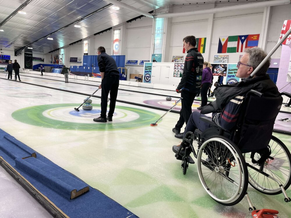 A three people during a curling game, including one person in a wheelchair.