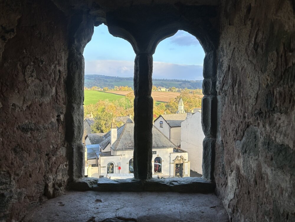 A view of a village and the countryside through a stone castle window.