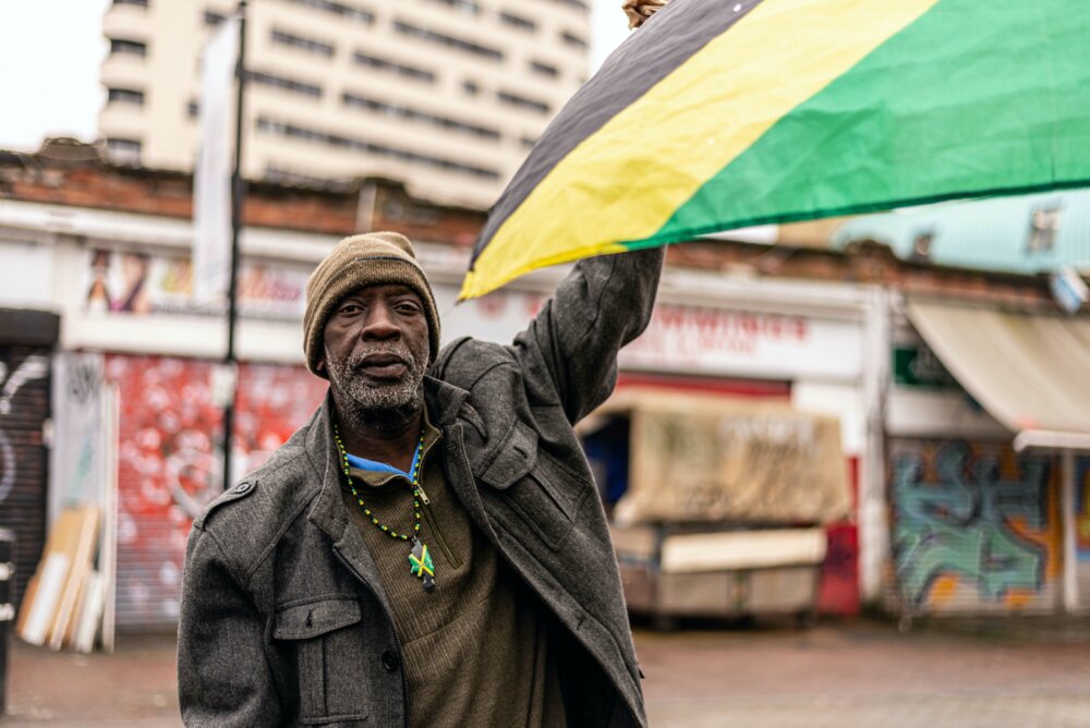 A man (Don Travis) with a Jamaican flag in Ridley Road, Hackney, London, England.