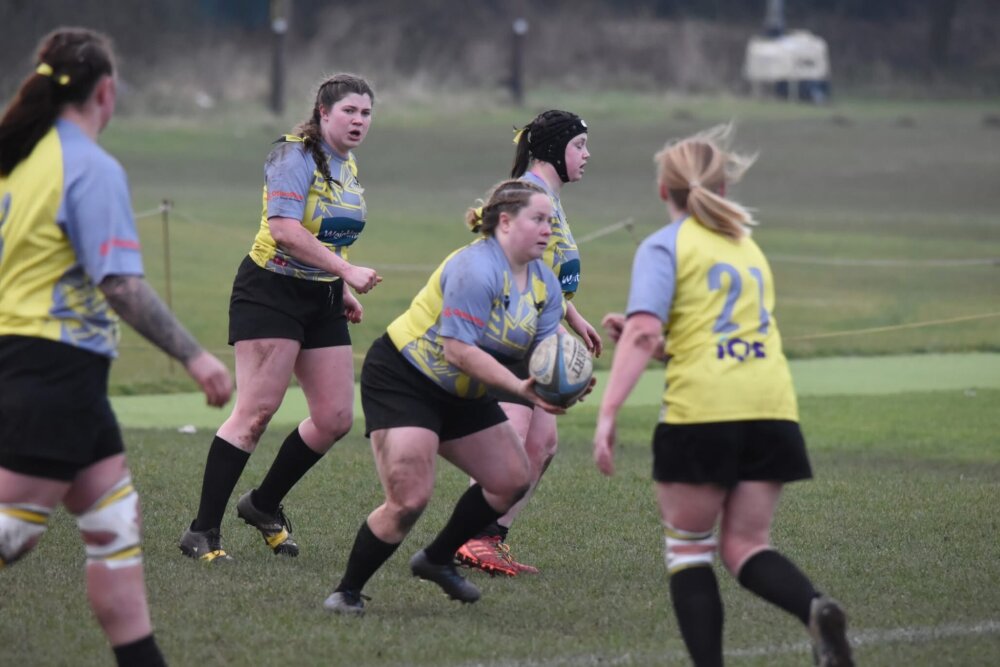 Five rugby players during a match, with one holding a rugby ball.