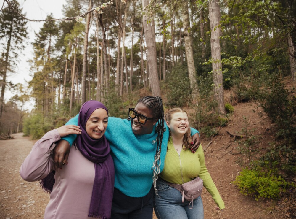 Three young people embracing and laughing while walking along a forest path.