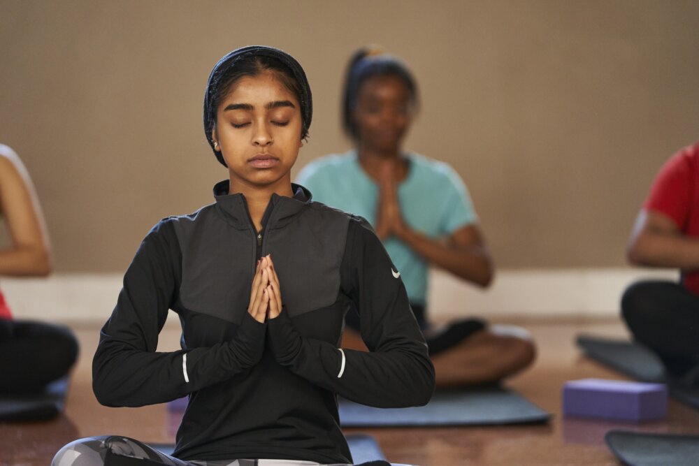 A woman sitting in a yoga pose with her eyes closed and hands together in a prayer position.