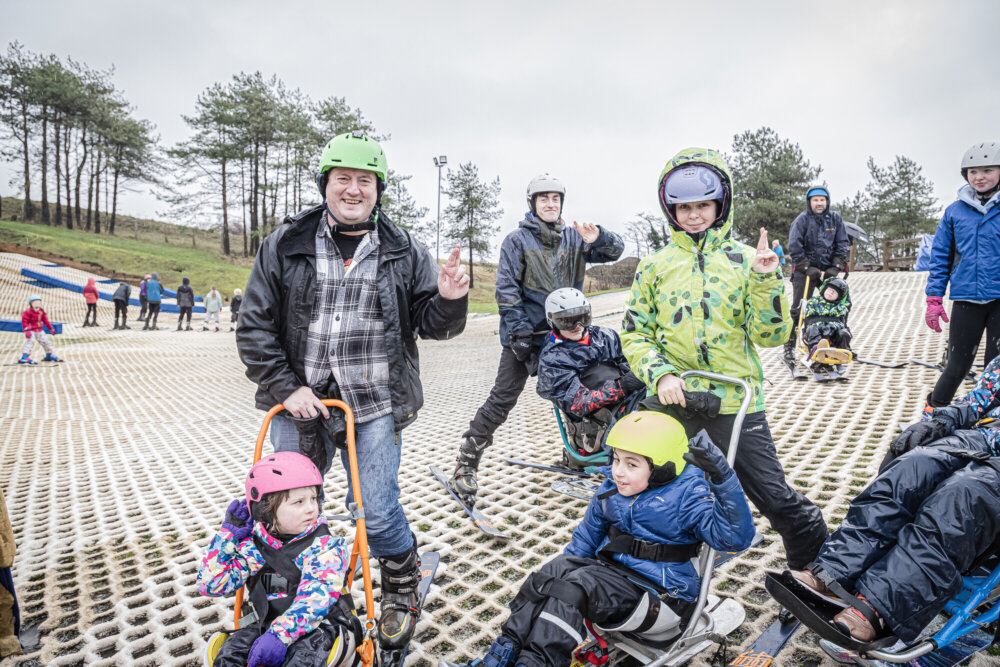 A young sit ski rider on the slope at Pembrey, guided by a club volunteer.