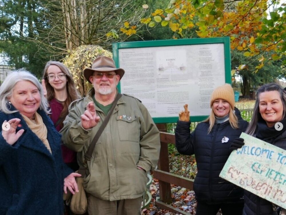 Five individuals standing outside holding up their fingers to the camera.