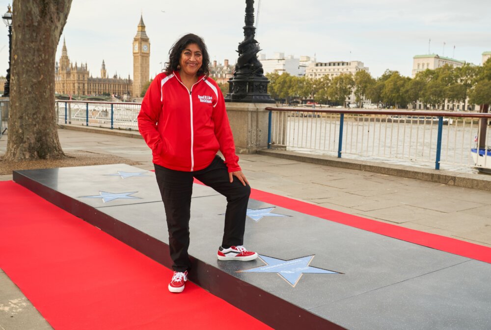 A woman, Gurinder Chadha OBE, next to stat on the floor of the National Lottery ‘walk of stars’ installation in London