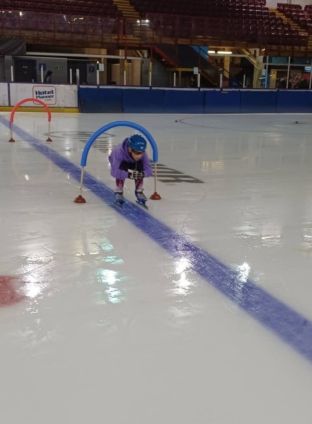 Photo of a youngster learning technique and skill, in a fun way, skating low under a barrier at an Altrincham Speed Skating Club session