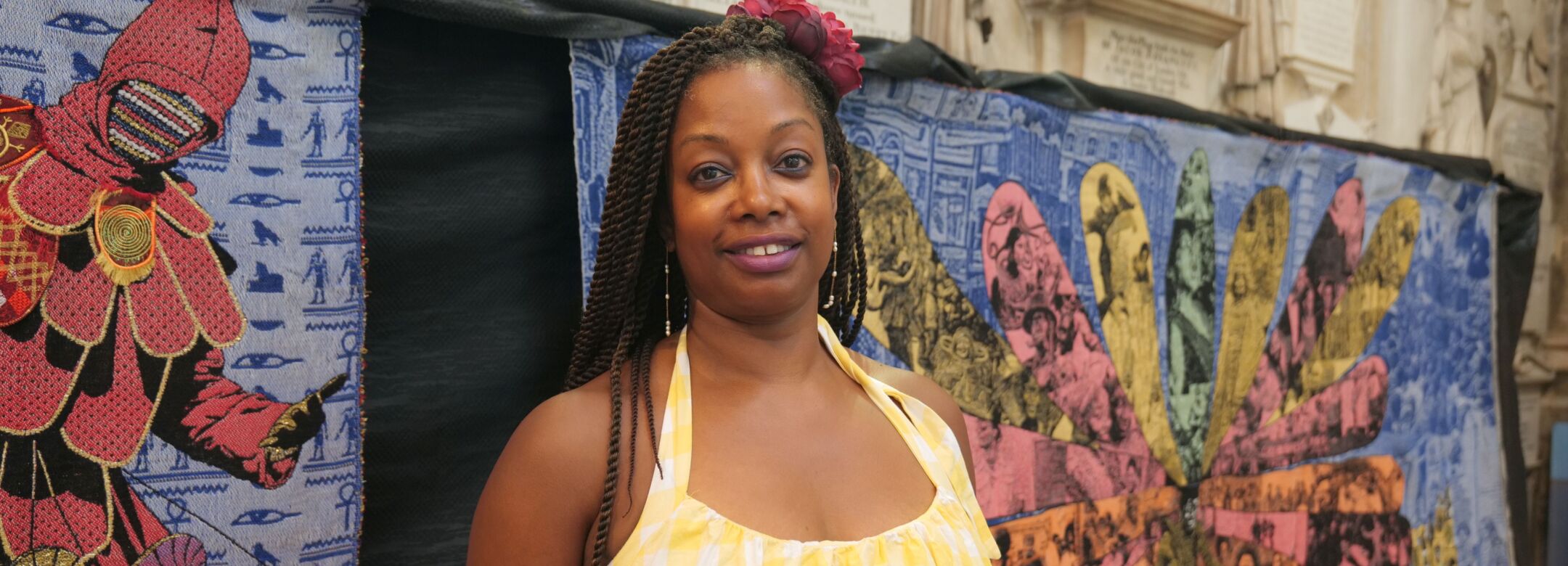 A person stands in front of a colourful textile artwork.