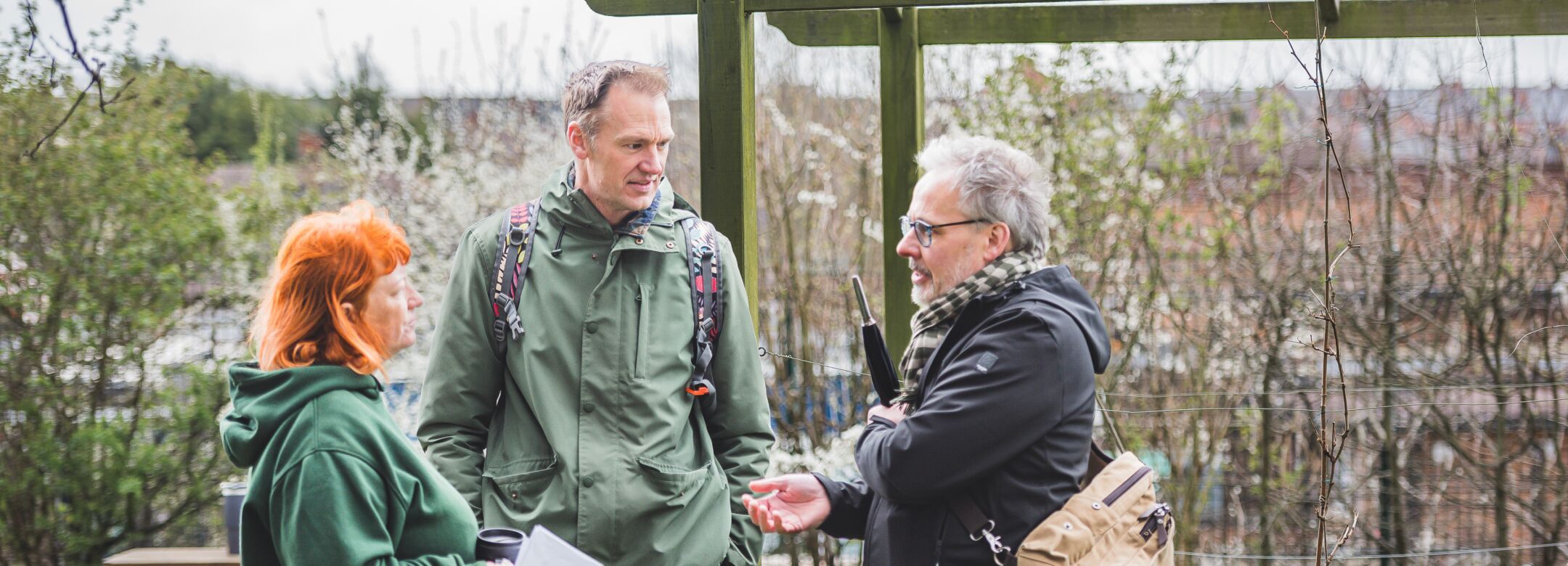 Three people standing in a garden, having a conversation.