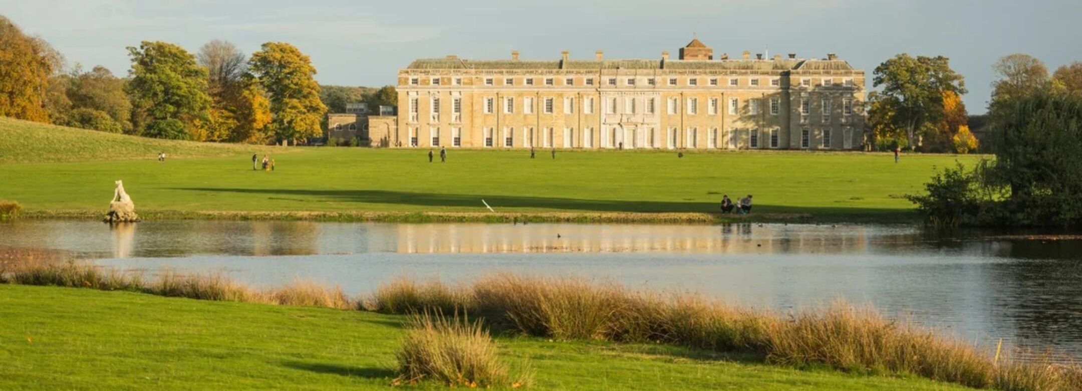 A large, old historic home surrounded by grass and a pond.