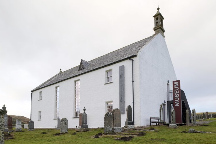 A white two storey church cited in a graveyard. A sign down the side reads 'museum'.