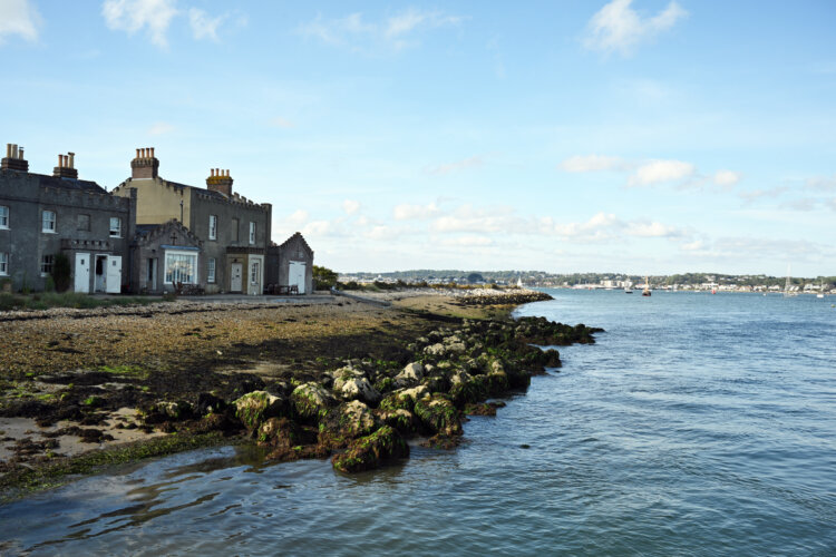 Two grey cottages sit at the end of a bay overlooking the sea and harbour in the distance