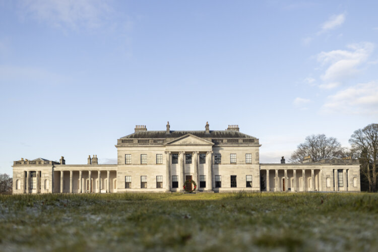 A large mansion with columns sits in the sun with blue skies