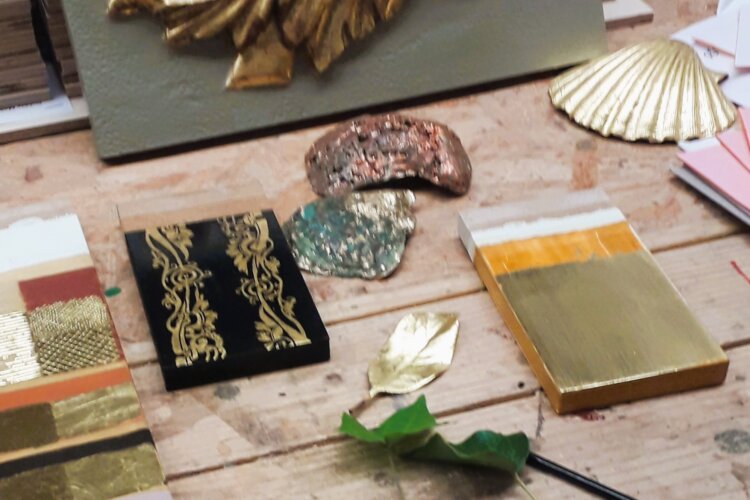 A craftsman's workbench with various samples and materials related to the art of gilding (the process of applying thin layers of gold leaf to surface)