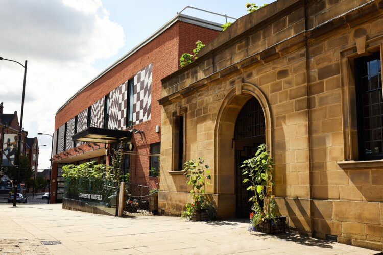 Exterior view of The Art House building on a city street, showing a historic stone entrance alongside a modern brick gallery with patterned window panel