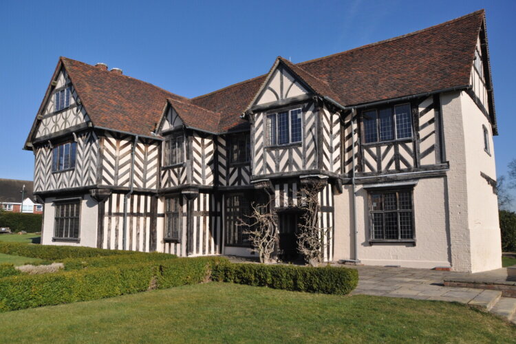 A tudor manor house set in green gardens on a sunny day