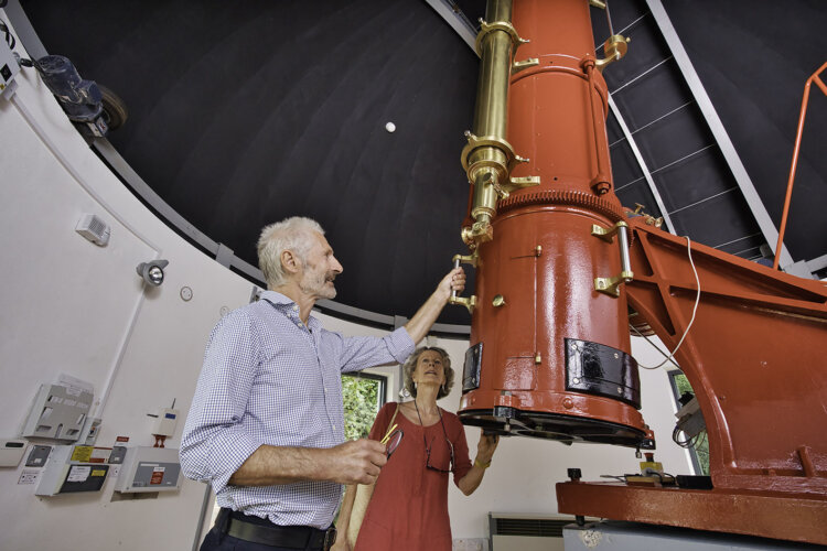 A man and woman observing a big red/brown telescope