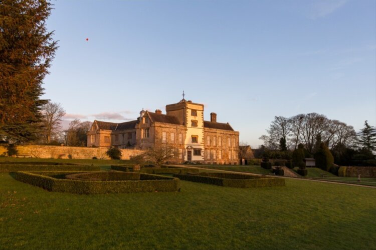 An old house at sunset with gardens and hedges at the front