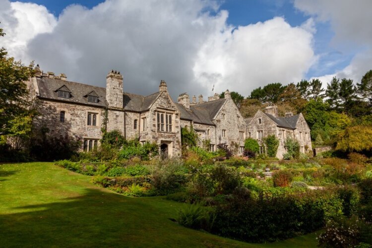 A blue but cloudy sky sits above an old country house with manicured gardens